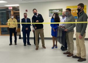 7 masked people at a ribbon cutting. One is holding a solar panel